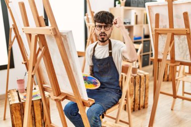 Sanat stüdyosundaki sakallı İspanyol adam öfkeyle bağırıyor, öfkeyle bağırıyor ve el kaldırıyor. 