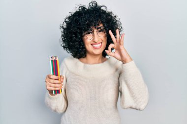 Orta Doğulu genç bir kadın elinde renkli kalemlerle işaret veriyor. Gülümsüyor. Mükemmel bir sembol. 