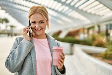 Sarışın iş kadını akıllı telefondan konuşuyor. Şehirde kahve içiyor..