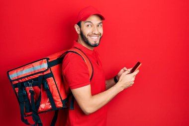 Sırt çantası takan İspanyol bir adam akıllı telefon kullanıyor. Gülümsüyor ve kafasını çeviriyor.. 