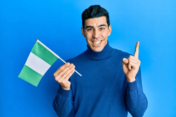 Hombre Hispano Guapo Sosteniendo Bandera Nigeria Sonriendo Feliz Señalando Con —  Fotos de Stock