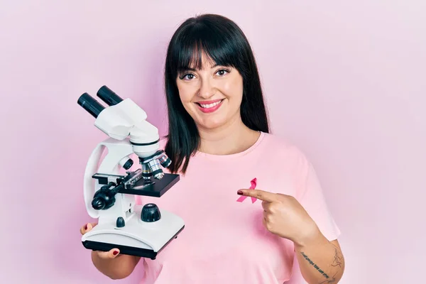 Mujer Hispana Joven Con Cinta Cáncer Rosa Camisa Sosteniendo Microscopio — Foto de Stock