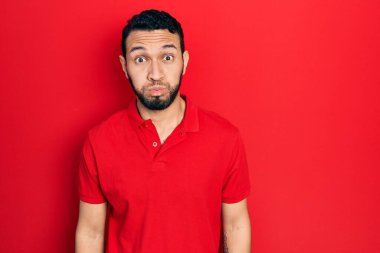 Sakallı, sıradan kırmızı tişörtlü, komik yüzlü İspanyol bir adam. Havayla şişmiş ağız, çılgın bir ifade.. 