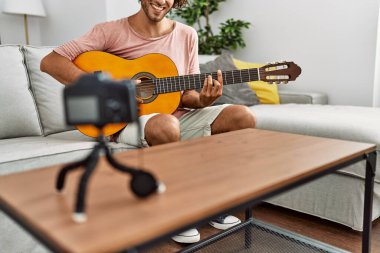 Evde klasik gitar çalan Latin asıllı genç bir adam kayıt yapıyor..