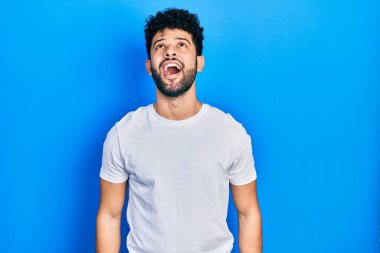 Sakallı, sıradan beyaz tişörtlü genç bir Arap sinirli ve öfkeli çığlıklar atıyor öfkeyle bağırıyor. öfke ve agresif konsept. 