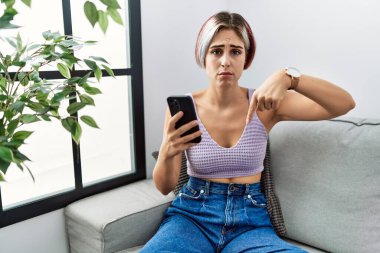 Genç ve güzel bir kadın akıllı telefon kullanarak kanepeye oturmuş üzgün ve üzgün bir şekilde işaret ediyor. Mutsuz ve depresif.. 