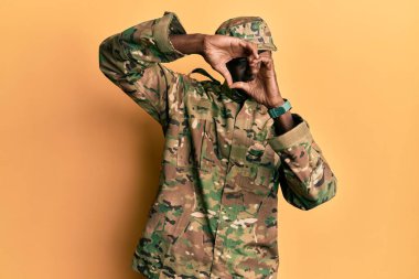 Asker üniforması giyen, elleri ve parmaklarıyla kalp şeklinde gülümseyen Afro-Amerikan bir adam. 