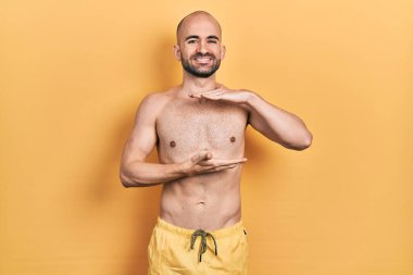 Elleriyle mayo giyen genç kel bir adam büyük ve büyük bir işaret, ölçü sembolü gösteriyor. Kameraya bakıp gülümsüyor. ölçüm kavramı. 