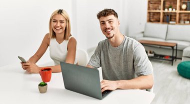 Kafkasyalı genç çift kahve içiyor ve evde dizüstü bilgisayar ve akıllı telefon kullanıyor..