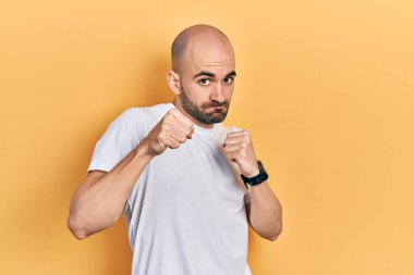 Genç, kel bir adam, günlük beyaz tişört giyiyor. Yumruk yumruğa dövüşüyor, agresif ve öfkeli saldırı, tehdit ve şiddet. 