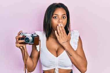 Genç Afro-Amerikalı kız elinde antika kamerayla ağzını eliyle kapatıyor, şok geçiriyor ve hata yapmaktan korkuyor. şaşırmış ifade 
