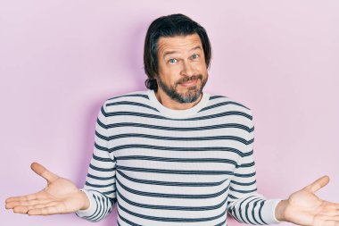 Orta yaşlı, sıradan kıyafetler giyen, elleri ve kolları havada, kafası karışmış bir beyaz adam. şüphe kavramı. 