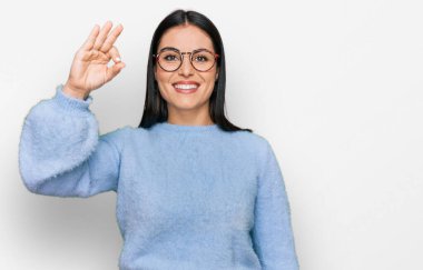 Gündelik kıyafetler ve gözlük takan genç İspanyol kadın gülümsüyor. El ve parmaklarıyla 