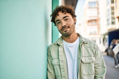 Yakışıklı, sakallı, güneşli bir günde mutlu bir şekilde gülümseyen bir İspanyol. Duvara yaslanmış.