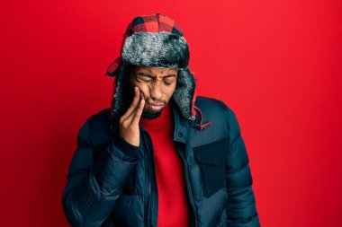 Sakallı, kışlık şapkalı ve paltolu genç Afro-Amerikan bir adam diş ağrısı ya da diş ağrısı yüzünden ağızlarına acı dolu bir ifadeyle dokunuyor. dişçi 