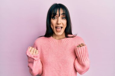 Kaküllü, sıradan bir kazak giyen genç esmer kadın kollarını kaldırarak ve açık gözlerle başarıyı kutluyor ve şaşırıyor. Kazanan konsept. 