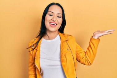 Burnu delinmiş, sarı deri ceketli, güzel İspanyol bir kadın. Gülümsüyor, eli avucunda kameraya bakıyor.. 