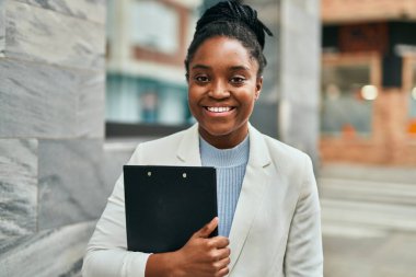 Genç Afrikalı Amerikalı iş kadını, şehirde elinde bir panoyla mutlu bir şekilde gülümsüyor..