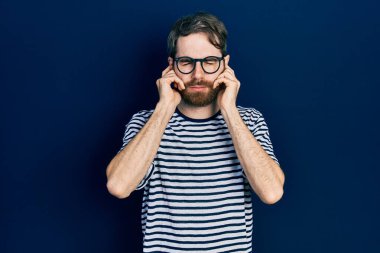 Beyaz sakallı, çizgili tişörtlü, gözlüklü, kulaklarını parmaklarıyla kapatan, gürültülü müzik sesi için rahatsız edici ifadeleri olan beyaz bir adam. sağır kavramı. 