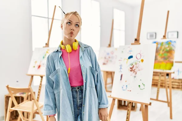 Young caucasian girl at art studio making fish face with lips, crazy and comical gesture. funny expression.