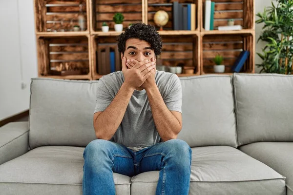 Ung Latinamerikan Klädd Vardagskläder Sittandes Soffan Hemma Chockad Täcka Munnen — Stockfoto