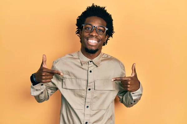 若いアフリカ系アメリカ人の男性は 笑顔で自信を持って見えるカジュアルな服や眼鏡を身に着けて 誇りに思って幸せな指で自分自身を指して — ストック写真