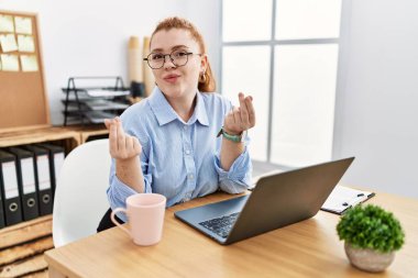 Ofiste çalışan genç kızıl saçlı bir kadın bilgisayar kullanıyor. Elleriyle para hareketi yapıyor. Maaş istiyor. 