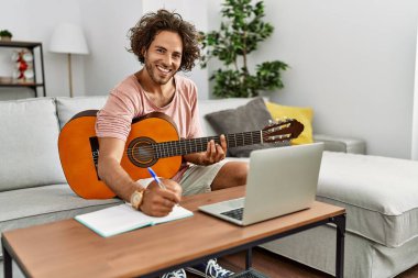 Genç İspanyol besteci evde gitar ve dizüstü bilgisayar kullanarak beste yapıyor..