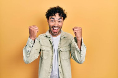 Gündelik giysiler giyen genç İspanyol adam şaşkınlık ve şaşkınlık içinde kollarını kaldırarak ve gözlerini açarak başarıyı kutluyor. Kazanan konsept. 