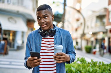 Genç Afrikalı Amerikalı adam akıllı telefon kullanıyor. Şehirde kahve içiyor..