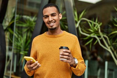 Genç Afrikalı Amerikalı adam akıllı telefon kullanıyor. Şehirde kahve içiyor..