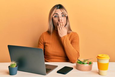 Ofiste çalışan beyaz bir kadın. Gözlük takıyor, ağzı ağızla kapanıyor. Şok olmuş ve hata yapmaktan korkuyor. şaşırmış ifade 