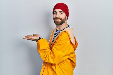 Sakallı, sarı yağmurluklu beyaz bir adam. Elleri açık, fotokopi alanını gösteren avuç içlerini gösteriyor. Gülümseyen mutlu bir gülümseme. 