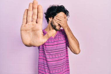 Yakışıklı, pembe tişört giyen, elleriyle gözlerini kapatan, üzgün ve korku ifadeli hareketler yapan bir İspanyol. utangaç ve olumsuz kavram. 