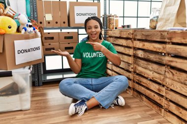 Bağışlarda gönüllü tişört giyen Afro-Amerikalı genç bir kadın hayret içinde durup kameraya gülümserken eliyle ve parmağıyla işaret ediyor.. 