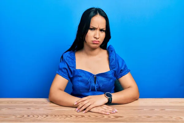 Beautiful hispanic woman with nose piercing sitting on the table skeptic and nervous, frowning upset because of problem. negative person.