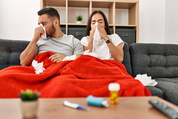 Young latin ill couple using napkin sititng on the sofa at home.