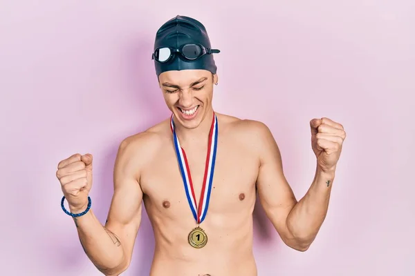 年轻的他惊慌失措的男人戴着泳镜 拿着金牌 高兴而兴奋地举起双臂 微笑着 尖叫着要成功 庆祝概念 — 图库照片