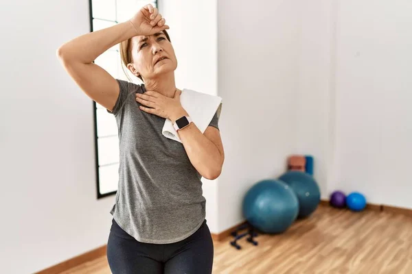 Middle age beautiful sportswoman wearing sportswear sitting on mat  practicing yoga at home crazy and mad shouting and yelling with aggressive  expression and arms raised. Frustration concept. Stock Photo