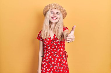 Sarışın, güzel, beyaz bir kadın. Yaz şapkası takıyor. Dostane bir şekilde el sıkışarak selam veriyor. başarılı iş. 