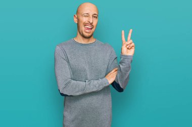 Sakallı, sıradan kıyafetler giyen, gülen, kameraya göz kırpan, zafer işareti yapan kel bir adam. İki numara.. 