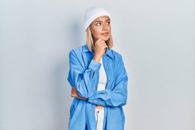 Güzel sarışın kadın, elleri çenesinde yün şapkalı soru soran, düşünceli bir ifade takınıyor. Gülümseyen ve düşünceli bir yüz. şüphe kavramı. 