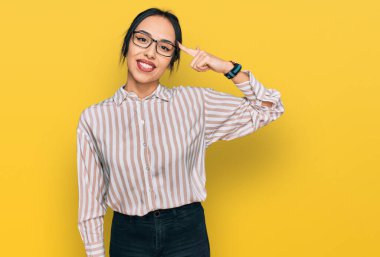 Gündelik kıyafetler ve gözlük takan genç İspanyol kız tek parmakla başını gösteren gülümseme, harika bir fikir ya da düşünce, iyi bir hafıza 