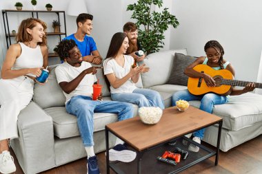 Mutlu gülümseyen ve evde klasik gitar çalan bir grup genç arkadaş..