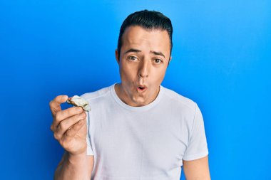 Yakışıklı genç adam çiğ istiridye tutuyor. Korkmuş ve ağzı açık kalmış, şaşırmış ve şaşırmış. 