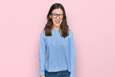 Gündelik kıyafetler giyen ve gözlüklü genç bir kadın kameraya seksi bir ifadeyle bakıyor, neşeli ve mutlu bir yüzle.. 