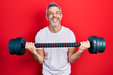 Yakışıklı, orta yaşlı, gri saçlı spor giysili, halterli, gülen, kahkahalar atan bir adam.. 