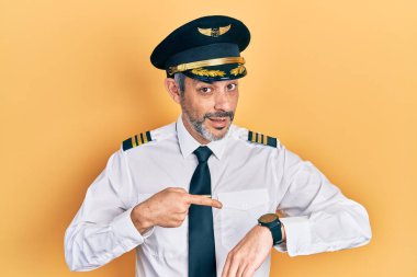 Gri saçlı yakışıklı orta yaşlı adam, uçak pilotu üniforması giyiyor. Aceleyle saati, sabırsızlığı, son teslim tarihini geciktirdiği için üzgün ve kızgın olduğunu gösteriyor. 