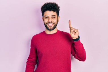 Sıradan pembe süveter giyen sakallı genç bir Arap başarılı bir fikri işaret ediyor. Heyecanlı ve mutlu. Bir numara.. 