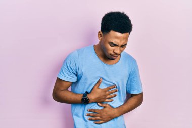 Genç Afro-Amerikalı adam, hazımsızlık, acı veren hastalıklar yüzünden elleri ve göbeği açık mavi tişört giyiyor. Ağrı kavramı. 